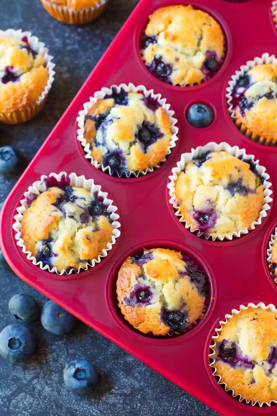 Freshly baked blueberry muffins cooling in a red muffin tray