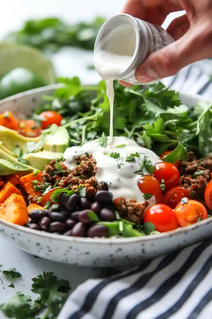 Hand pouring garlic lime dressing over a sweet potato taco bowl